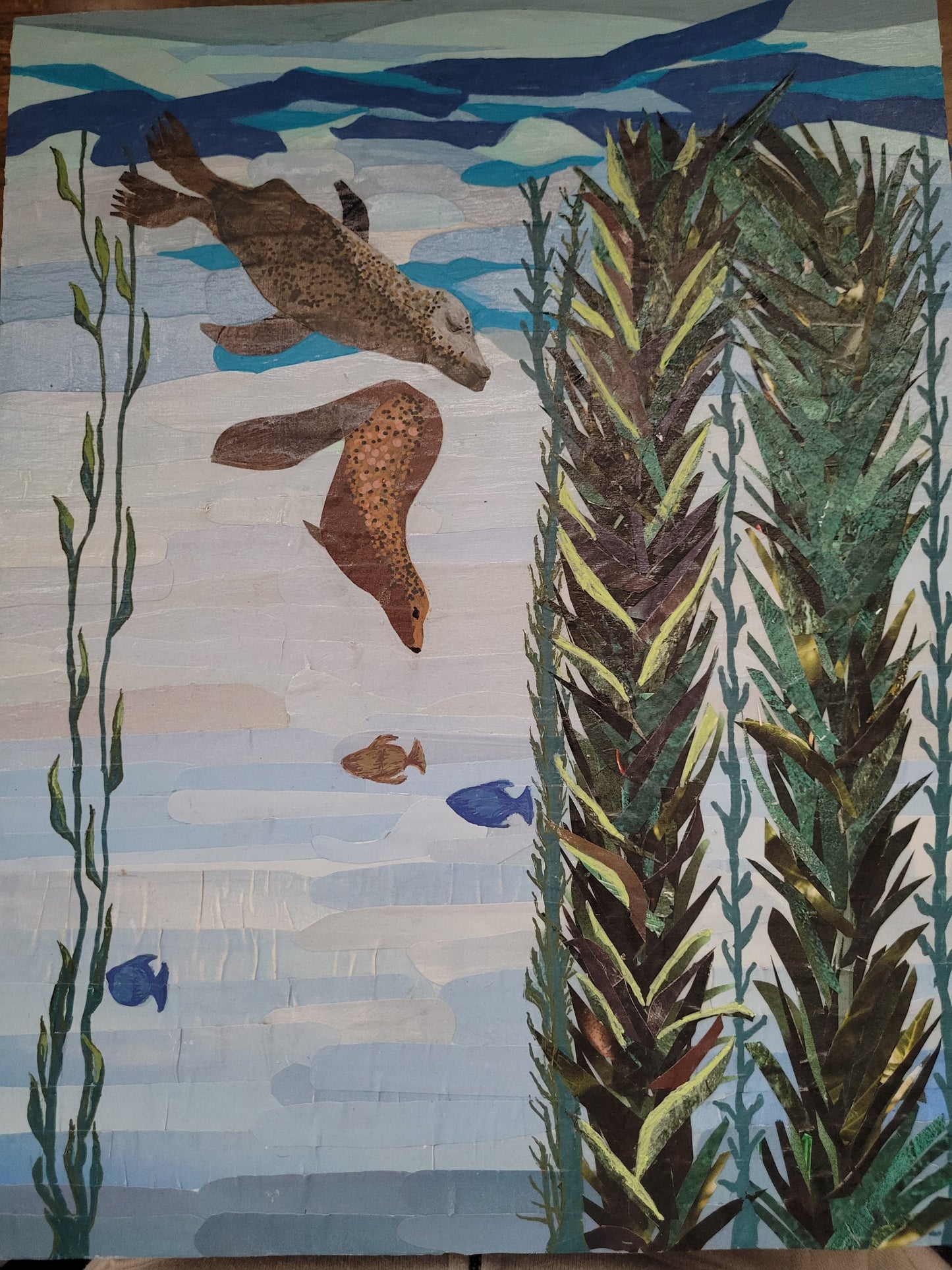 Work-in-progress view of Playful by Dawn Leigh, showing hand-cut reclaimed paper harbor seals and kelp being layered into an underwater scene.